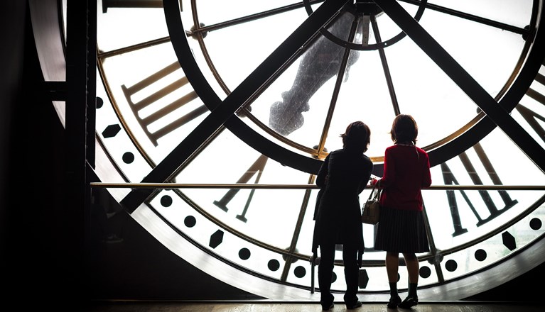 Bild som visar två kvinnosiluetter som står inuti en stor klocka.