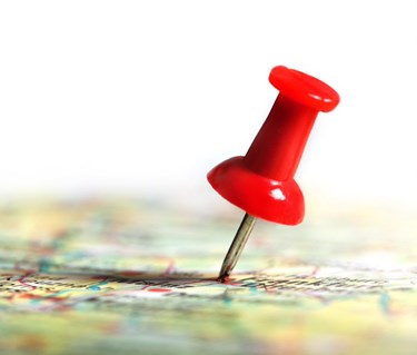 Bild med en röd nål på en karta i färg.