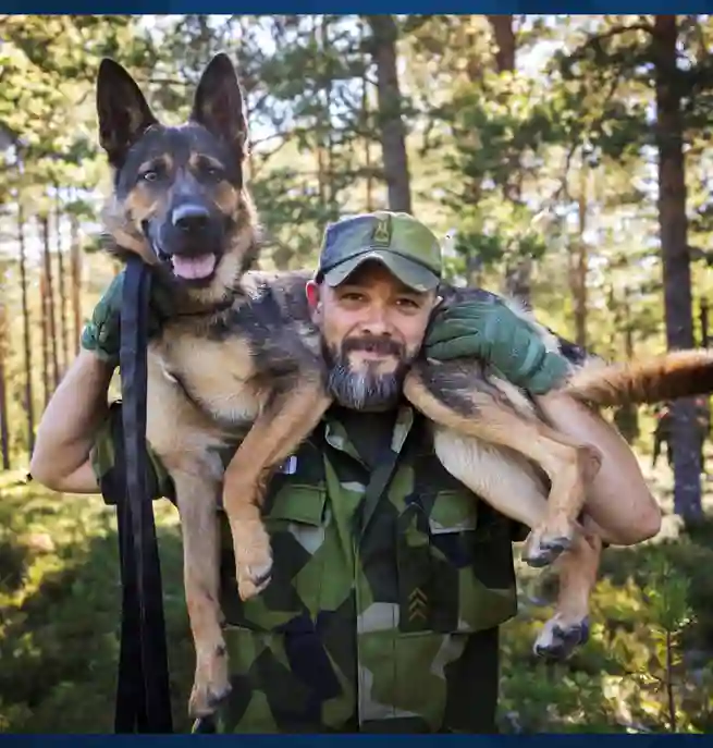 Man i svensk militäruniform ler mot kameran med en schäfer på sina axlar 