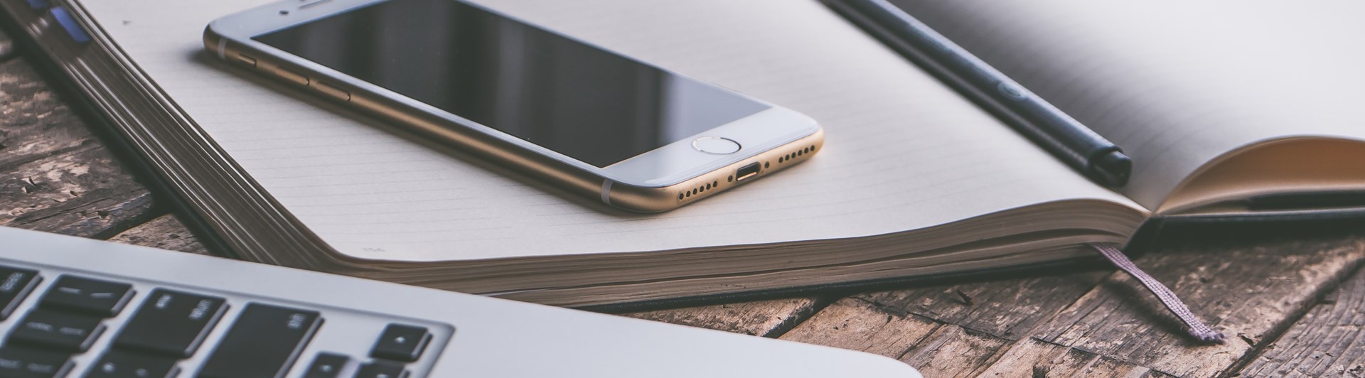 Bild på administrationsarbete med bärbardator, mobil och anteckningsblock.