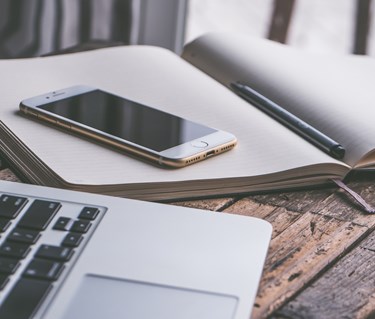 Bild på administrationsarbete med bärbardator, mobil och anteckningsblock.