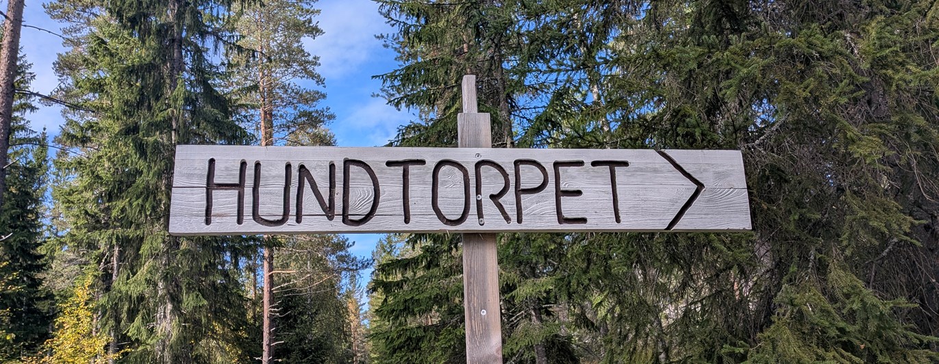 Skylt i trä med texten Hundtorpet och en pil.