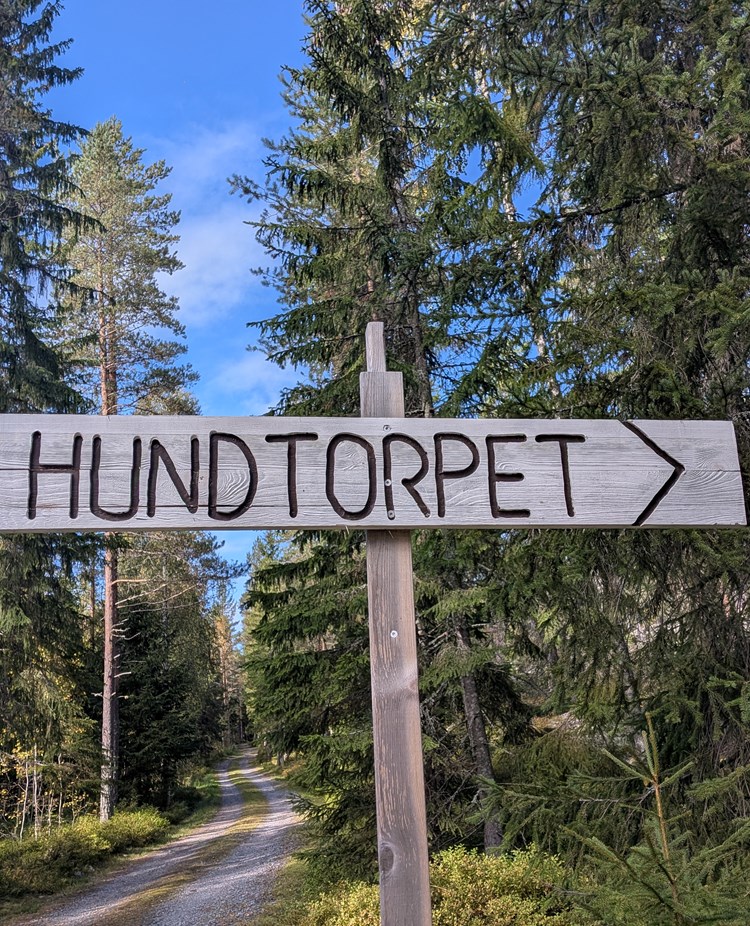 Skylt i trä med texten Hundtorpet och en pil.