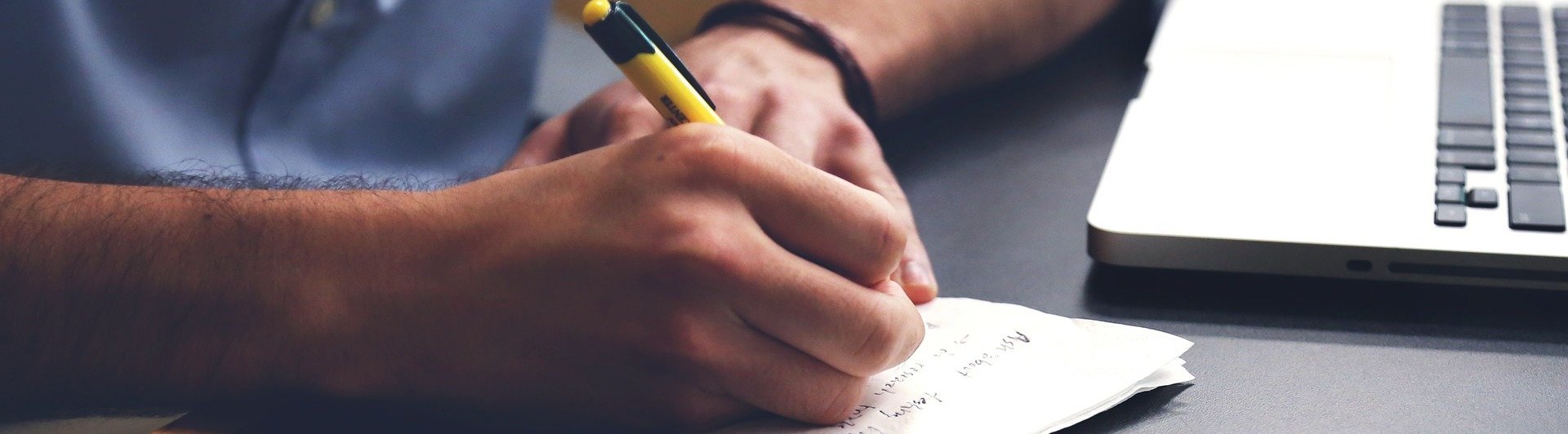 En man skriver på ett block bredvid en dator
