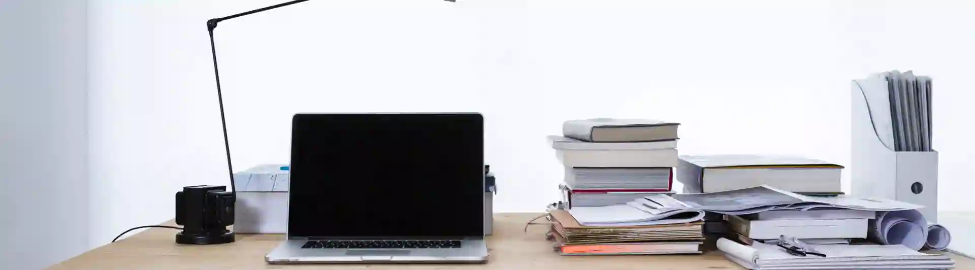 Bild som visar arbetsplats med bärbar dator, papper, dokument och böcker.