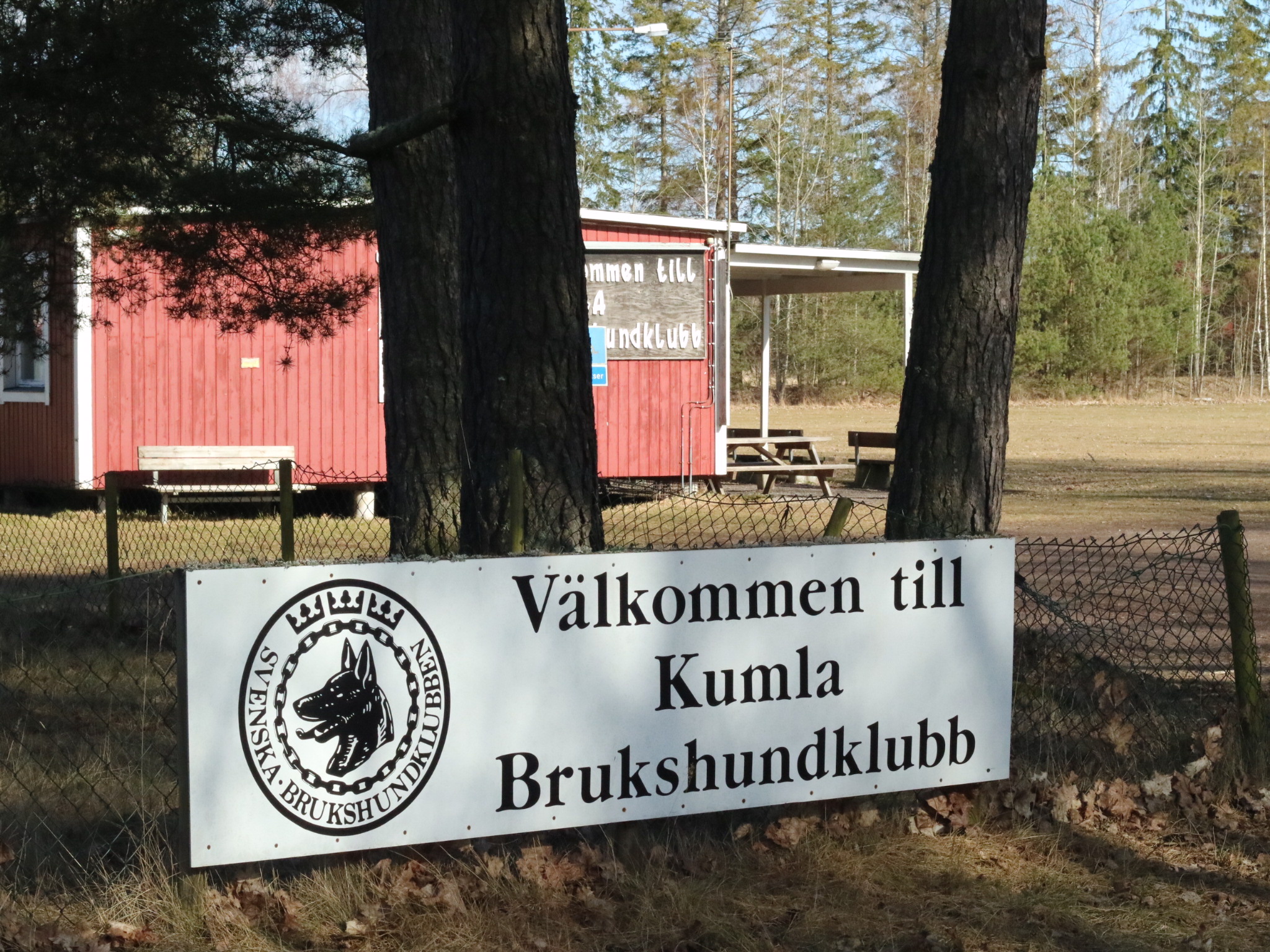 En skylt på Kumla brukshundklubbs klubbstuga och appellplan en solig dag