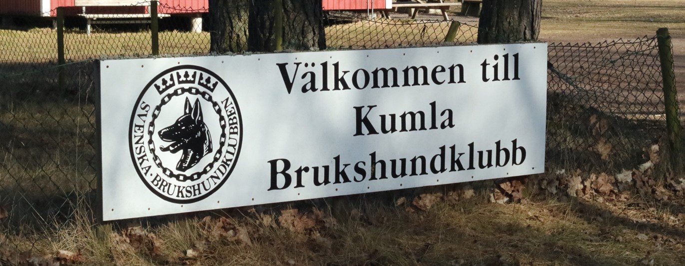 En skylt på Kumla brukshundklubbs klubbstuga och appellplan en solig dag