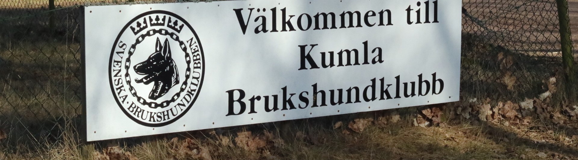 En skylt på Kumla brukshundklubbs klubbstuga och appellplan en solig dag