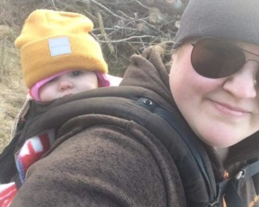 En tjej som är ute och går med sitt barn på ryggen.